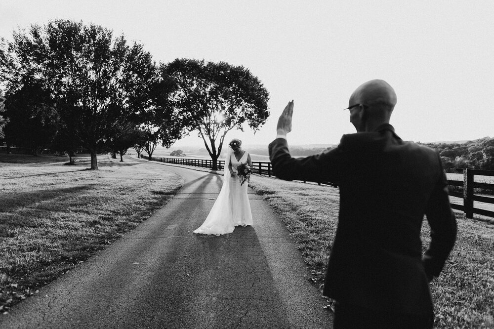 Classy black and white image at Ironwood in Bowling Green of bride wearing long veil standing in the road while the sun sets with the groom in the foreground.