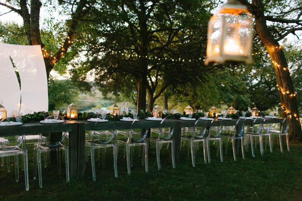 Backyard wedding reception in Nashville, Tennessee with farmhouse table, clear chairs, lanterns, string lights, and greenery.