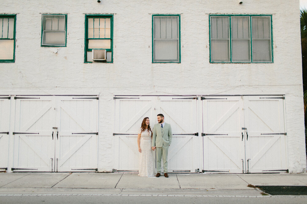 Bride and groom dressed in a pale green suit holding hands in front of white barn doors in Delray Beach, Florida.