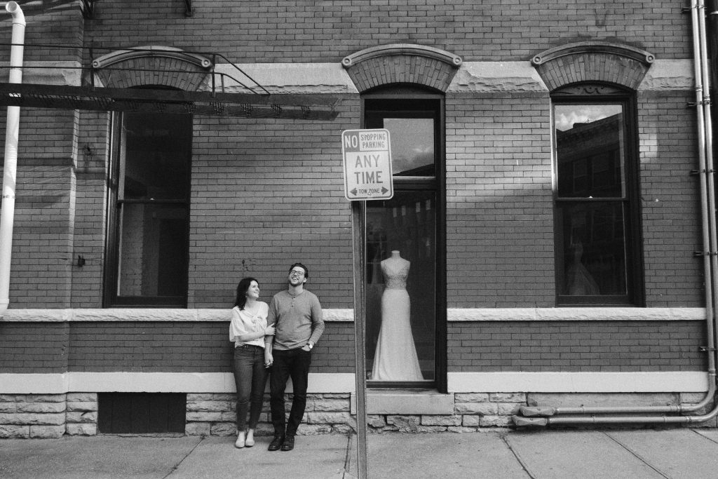 Black and white photo of young couple holding hands and laughing against brick wall in Cincinnati, Ohio.